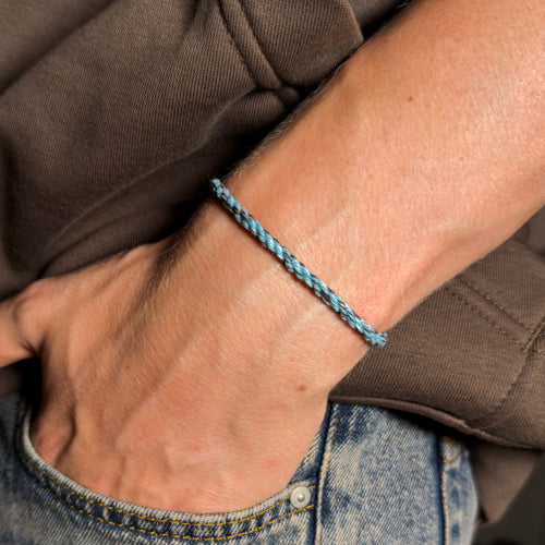 Close-up of a wrist wearing a blue bracelet made from a pets collar with a brown jacket and jeans in the background.